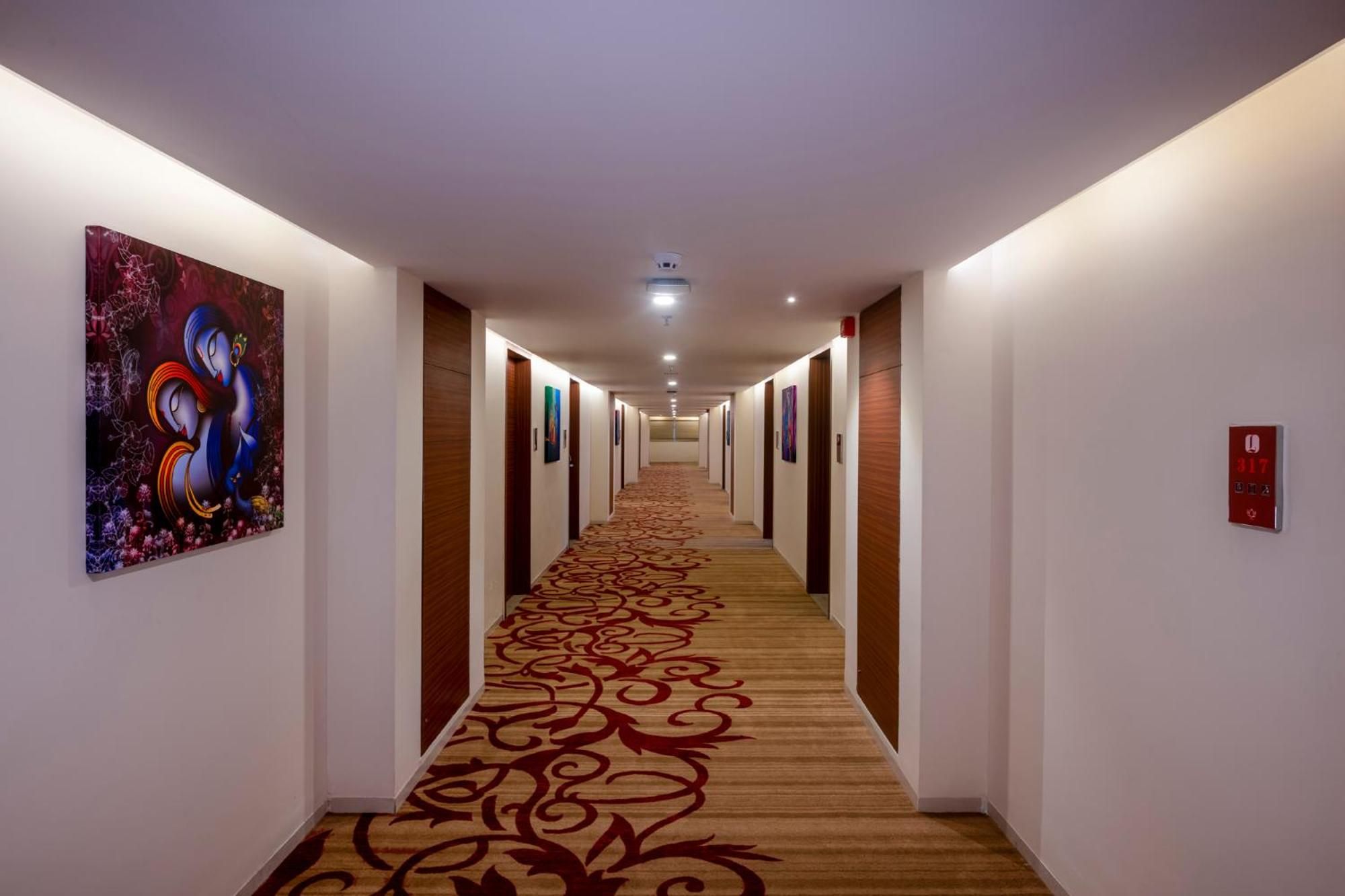 Un pasillo de hotel con piso alfombrado, puertas a ambos lados y obras de arte en las paredes.