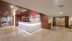Eine Hotelrezeption im modernen Design mit Empfangsschalter, Wanduhr und einer Zimmerpflanze.