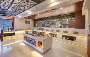 Um lobby de hotel moderno com área de buffet central, parede estampada e vista para a paisagem urbana através de grandes janelas.