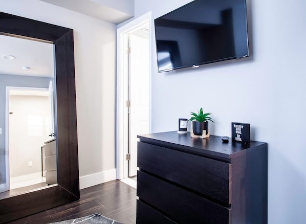 A modern interior with a dark wooden dresser, a flat-screen TV mounted on the wall, and a small potted plant on the dresser.
