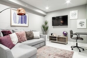 A modern living room with a grey sofa, a flat-screen TV, a globe, and a desk with a chair.
