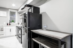 A modern kitchen with a built-in oven, a black refrigerator, and a wooden table with a metal frame.