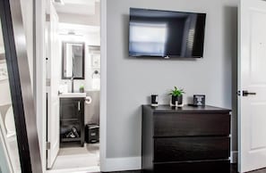 A modern bathroom with a dark wooden vanity, a mounted TV, and a small plant.