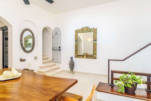 Une pièce spacieuse avec une table à manger en bois, un escalier agrémenté d’une porte décorative et un grand miroir doté d’un cadre orné.