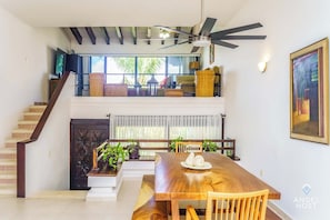 Un vaste espace de vie comprenant une table à manger en bois, un escalier menant à une mezzanine et un ventilateur de plafond.