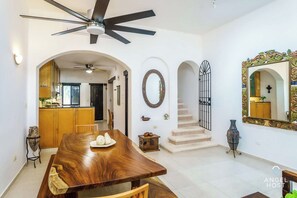 A spacious dining area with a wooden table and chairs, a ceiling fan, and a kitchen in the background.