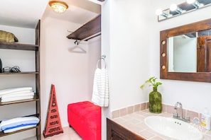 A bathroom with a sink, mirror, towel rack, and a red bench.