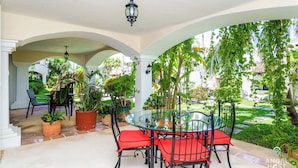 A covered patio with a glass table and red chairs, surrounded by potted plants and columns. - Lagoon Views with Beach Access, Pool and Patio (Cancún Q.R)