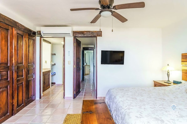 A bedroom with a bed, a ceiling fan, a TV, and wooden doors.