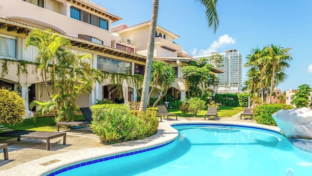 A pool area with lounge chairs, palm trees, and a building with balconies. - Lagoon Views with Beach Access, Pool and Patio (Cancún Q.R)