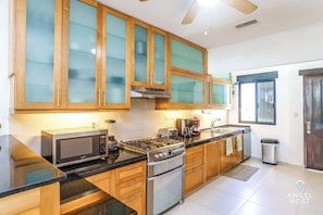 A modern kitchen with wooden cabinets, a stove, a microwave, and a coffee maker. - Hotel Zone Stay with Lagoon Views and Pools (Cancún Q.R)