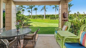 Un porche techado con mobiliario de mimbre, una mesa con una orquídea en maceta y vistas a un campo de golf.
