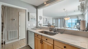 Una cocina moderna con una isla grande, armarios de madera y un espejo amplio que refleja el ambiente.