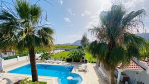 Una piscina con sillas de descanso, rodeada de palmeras y un césped bien cuidado.