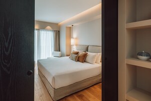 Camera d'albergo con un letto grande, un comodino, una lampada e vista all'esterno attraverso una finestra con tende.