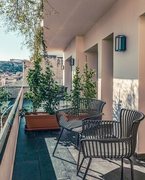 A balcony with two chairs and potted plants, overlooking a cityscape.