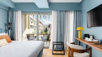 Une chambre d’hôtel avec un lit, un bureau doté d’une lampe, une chaise et une vue sur la ville grâce à de grandes fenêtres.