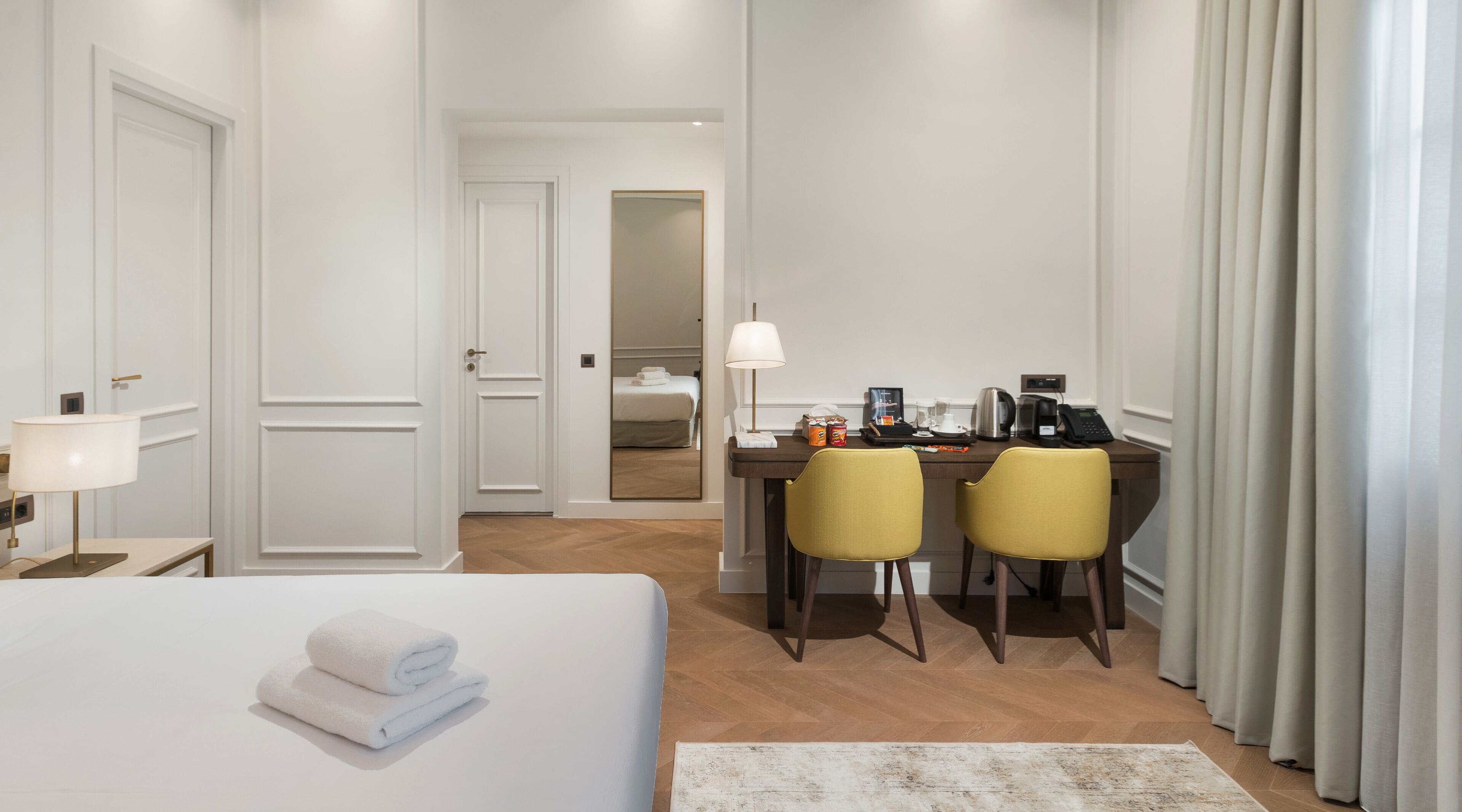A hotel room with a bed, a desk with two chairs, a lamp, and a coffee maker.