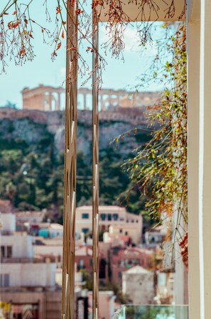 A view through a window with a balcony, featuring a cityscape with buildings and a distant structure on a hill.