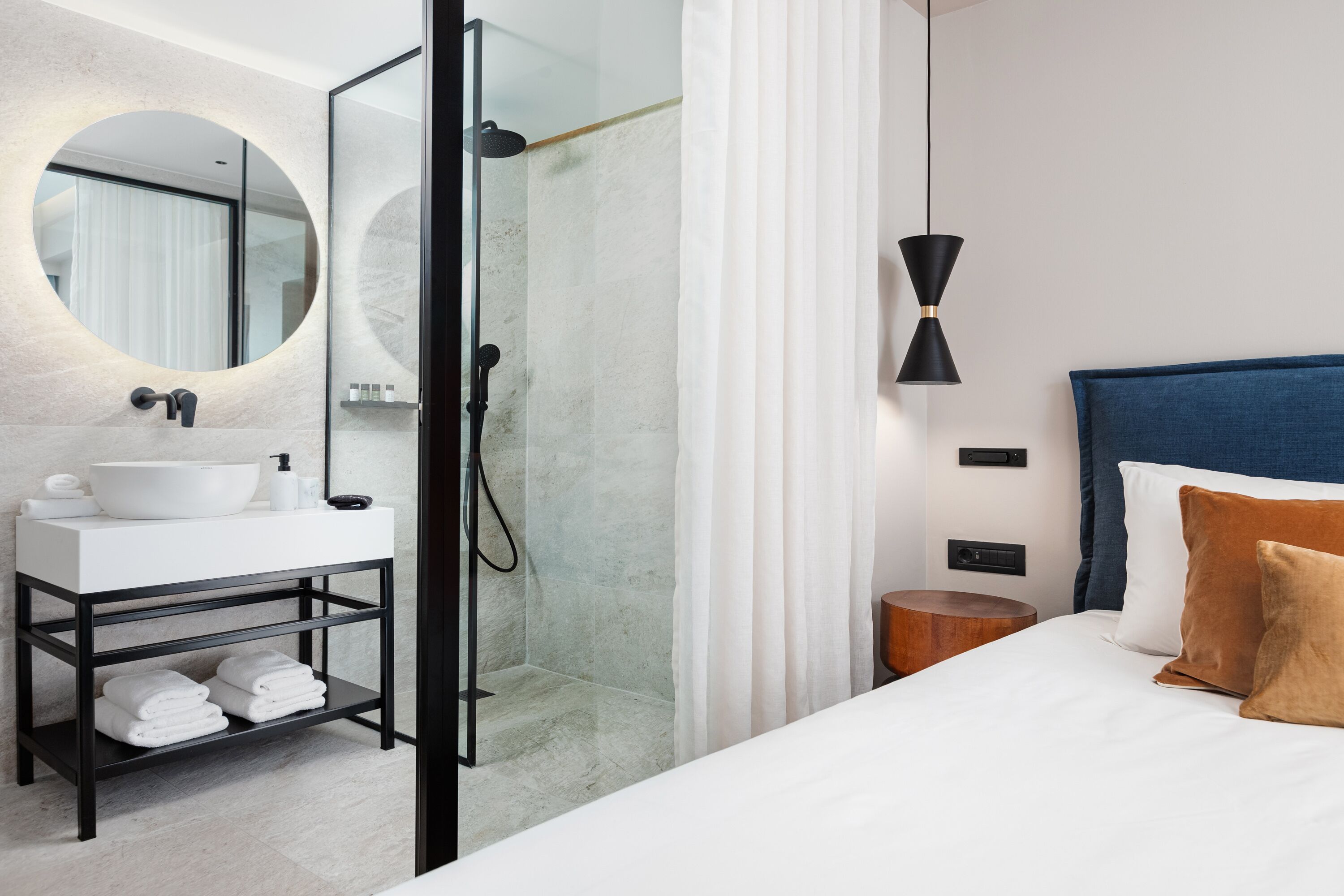 A modern bathroom with a round mirror, white sink, and a glass-enclosed shower.
