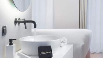 Un bagno moderno con un lavandino bianco, uno specchio grande, un asciugamano e una bottiglia di sapone.