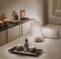 Un cuarto de spa con una camilla de masaje, una pequeña estatua de Buda y dos velas decorativas sobre una bandeja.