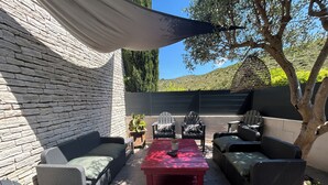 Um pátio externo com móveis de vime, uma mesa vermelha e uma pérgula que oferece sombra.