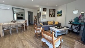 Uma sala de estar moderna com área de jantar, piso de madeira e uma variedade de móveis, incluindo um sofá, cadeiras e uma mesa de centro.