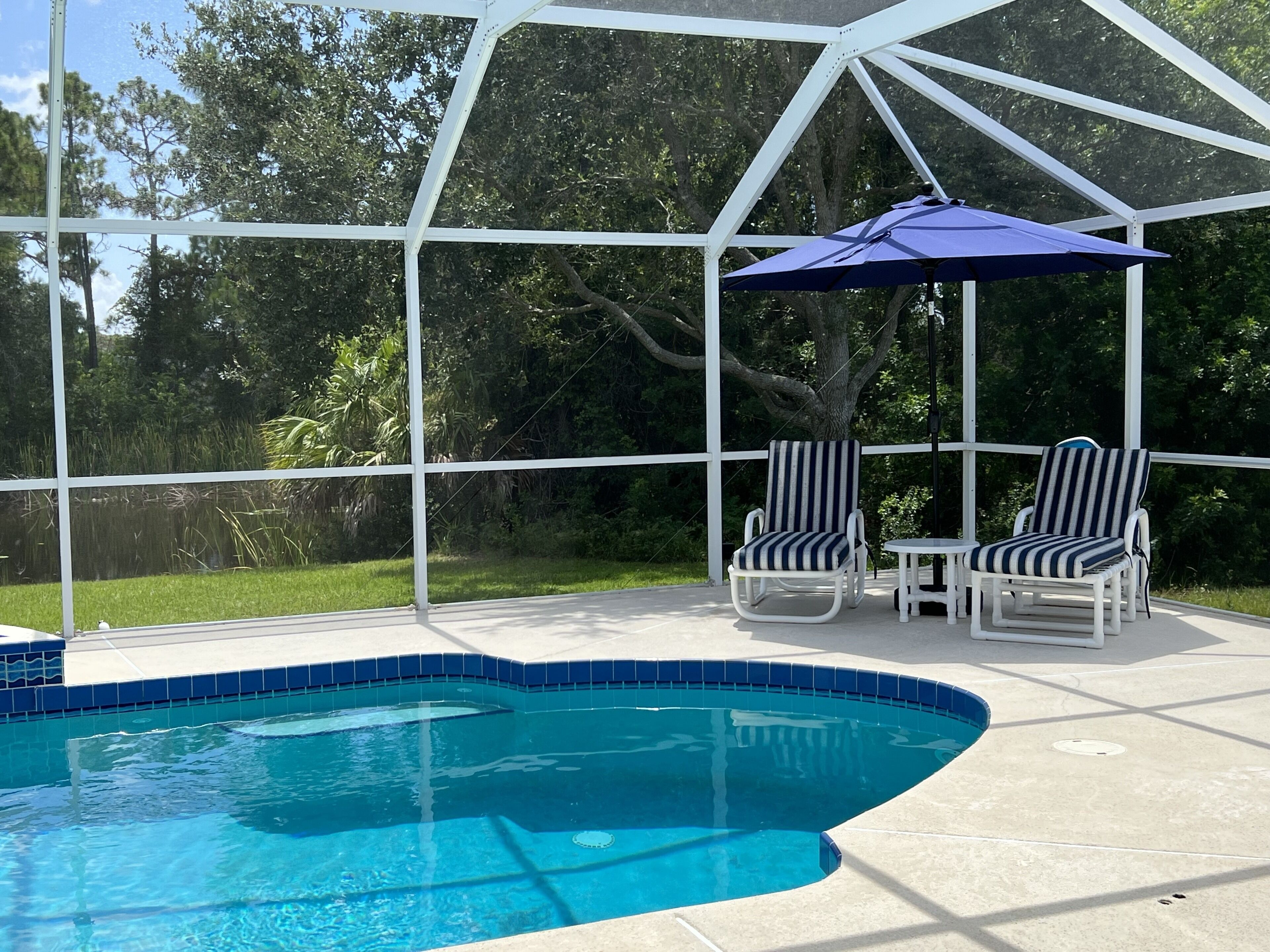 A covered outdoor swimming pool with two lounge chairs and a blue umbrella.
