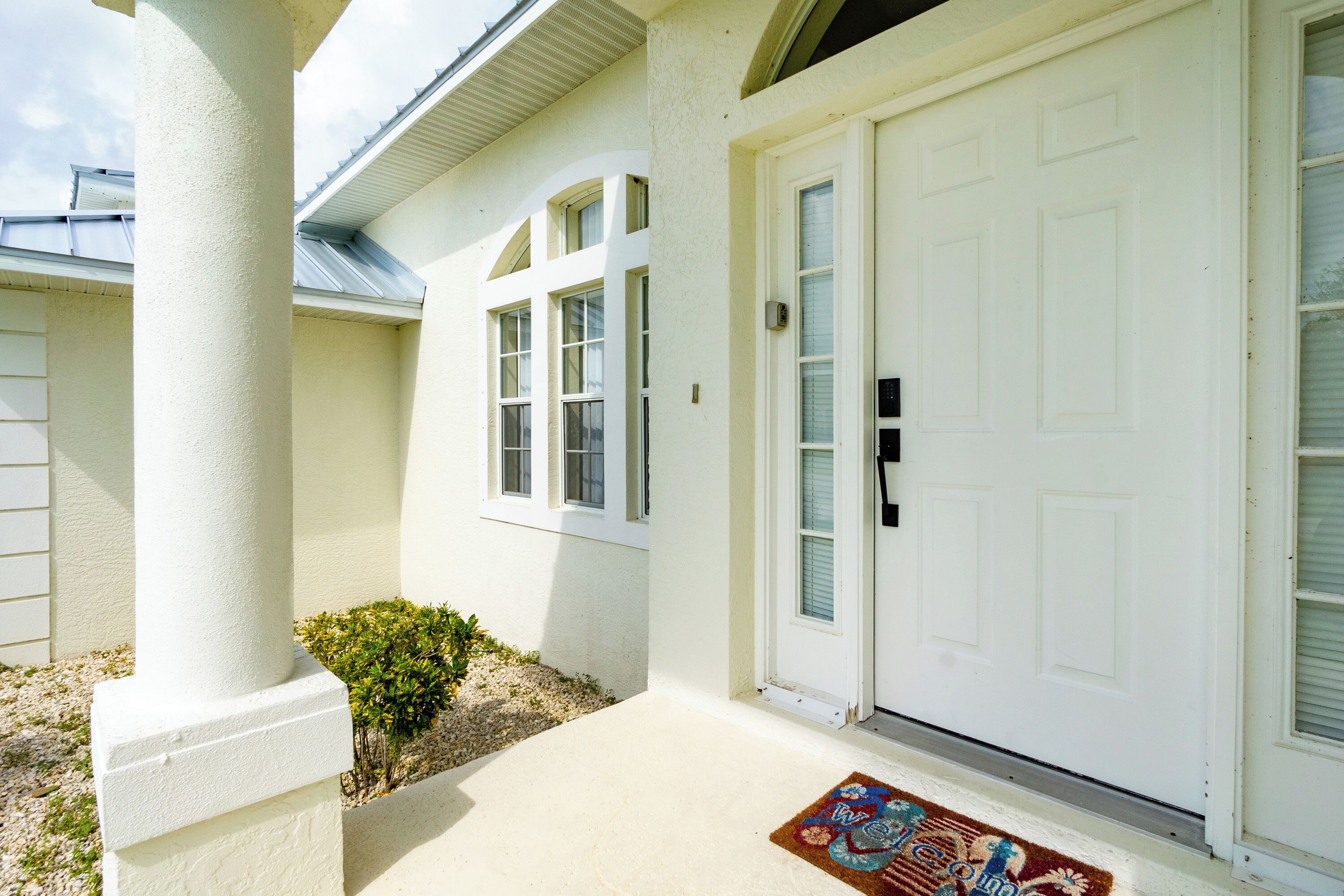 Une maison blanche avec une porte d’entrée, des fenêtres et un petit jardin.