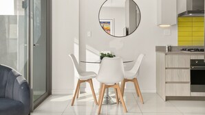 Una cocina moderna con un espejo redondo, armarios blancos y un comedor con mesa de vidrio y sillas blancas.