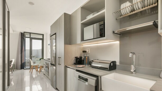 Una cocina moderna con lavavajillas, cafetera y tostadora. Se ve un comedor con una mesa y sillas a través de una puerta abierta.
