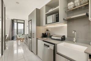 Una cocina moderna con lavavajillas, cafetera y tostadora. Se ve un comedor con una mesa y sillas a través de una puerta abierta.