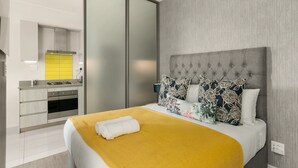 Una habitación de hotel moderna con cama, mesita de noche, cocina integrada con estufa y armario con puerta corredera.