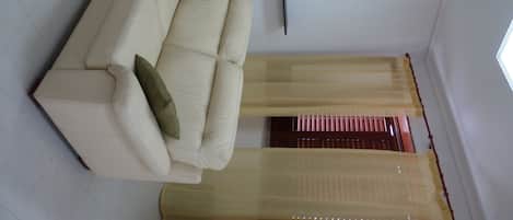 A living room with a beige sofa, a green pillow, a wall-mounted TV, and sheer curtains.