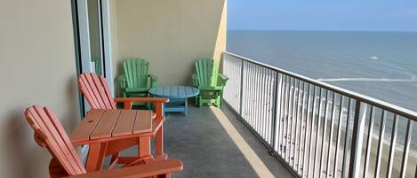 Uma varanda com mesa e cadeiras, vista para o oceano, e um corrimão.