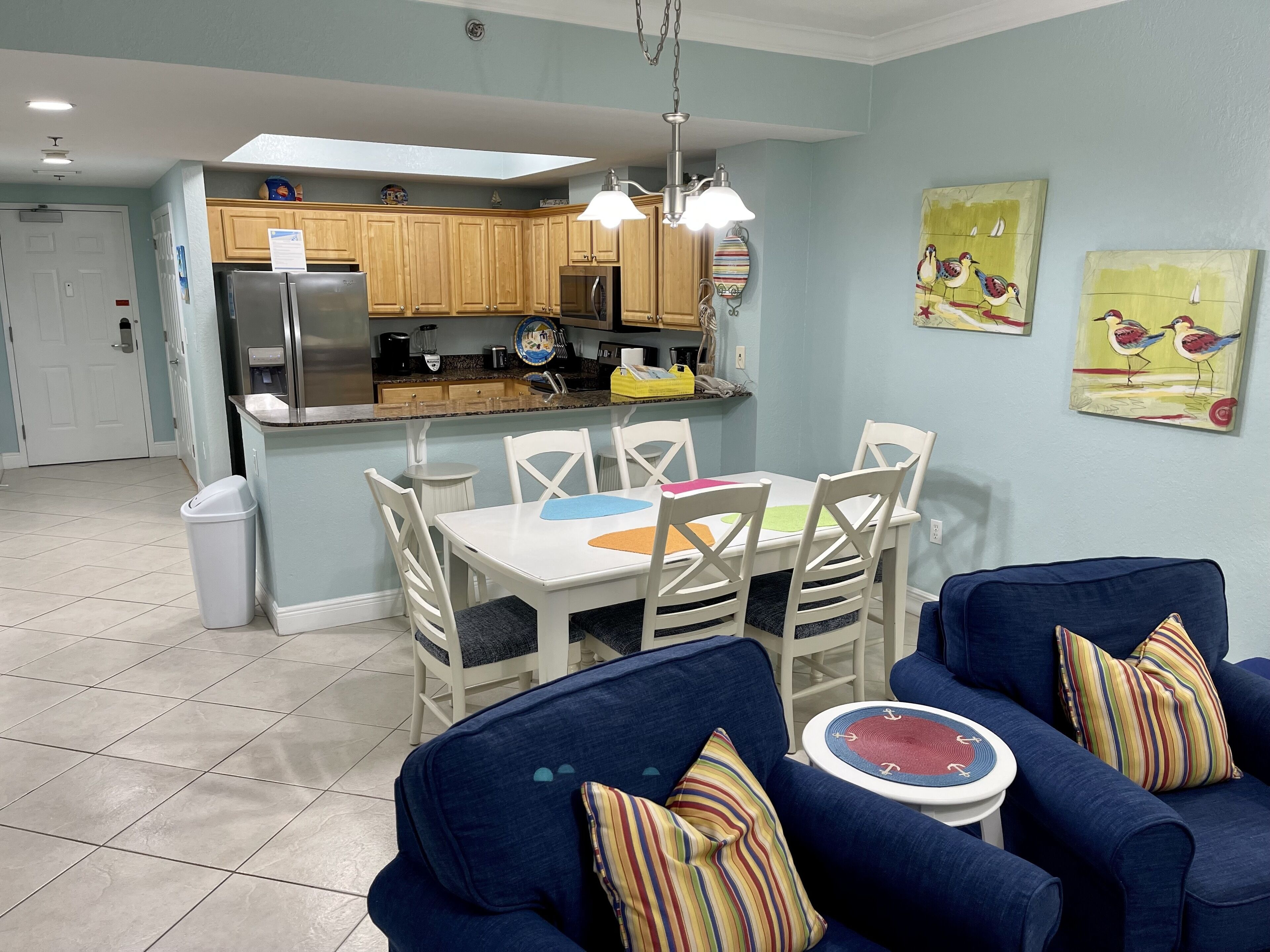 A modern kitchen with wooden cabinets, a refrigerator, and a dining area with a table and chairs.