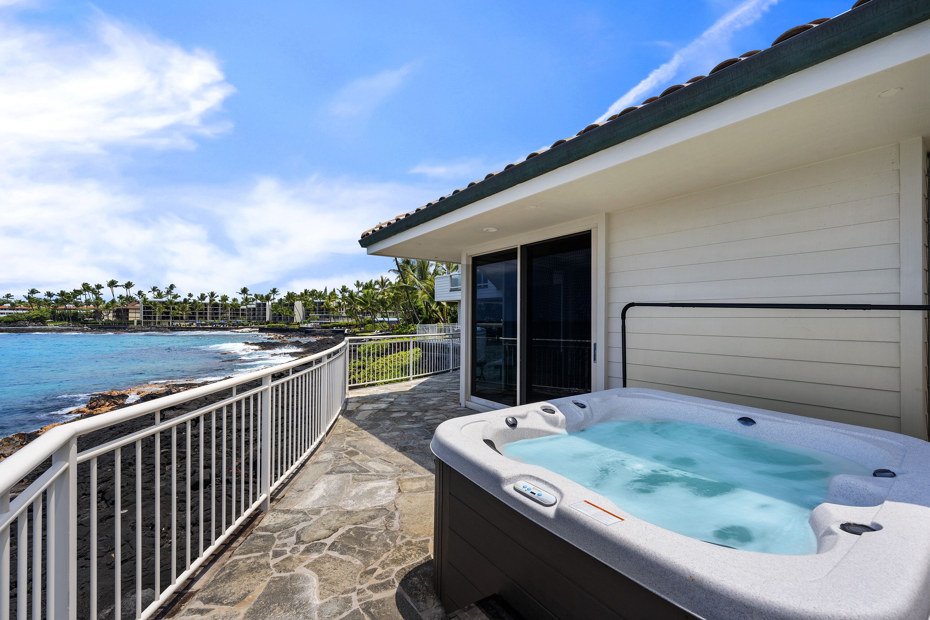 A hot tub on a stone deck with a view of the ocean and palm trees.