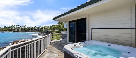 A hot tub on a stone deck with a view of the ocean and palm trees.