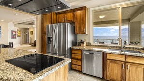 Una cocina moderna con electrodomésticos de acero inoxidable, encimeras de granito, armarios de madera y vistas al exterior.