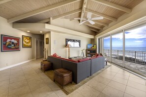 A spacious living area with a large window overlooking the ocean, a ceiling fan, and a seating area with a view.