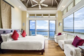 A bedroom with a large bed, two white sofas, and a view of the ocean.