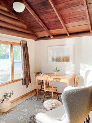 Une pièce chaleureuse avec un plafond en bois, une table à manger avec des chaises, une plante en pot et une vue sur l’extérieur par une fenêtre.