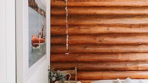 Acogedora habitación tipo cabaña con techo de madera, una cama, una silla con una cesta y un cuadro enmarcado en la pared.