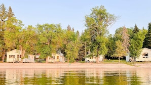 Cabañas en fila a orillas de un lago, con reflejos nítidos, rodeadas de árboles.