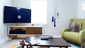 Una sala de estar con televisor de pantalla plana, un sillón verde, una mesa de centro y un atrapasueños.