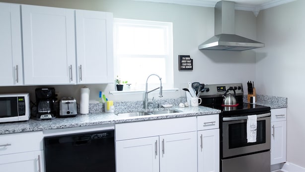 Una cocina moderna con armarios blancos, extractor de acero inoxidable, microondas, lavavajillas y encimera de granito.