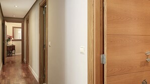 Ein Flur mit Holzboden, einer Holztür rechts und einem kleinen Tisch mit Blumen im Hintergrund.