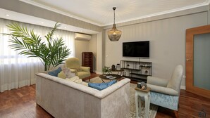 Ein Wohnzimmer mit Sofa, Sessel, Fernseher und einer großen Pflanze.