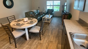 A compact living space with a dining area, a sofa, a coffee table, and a kitchen with a sink.